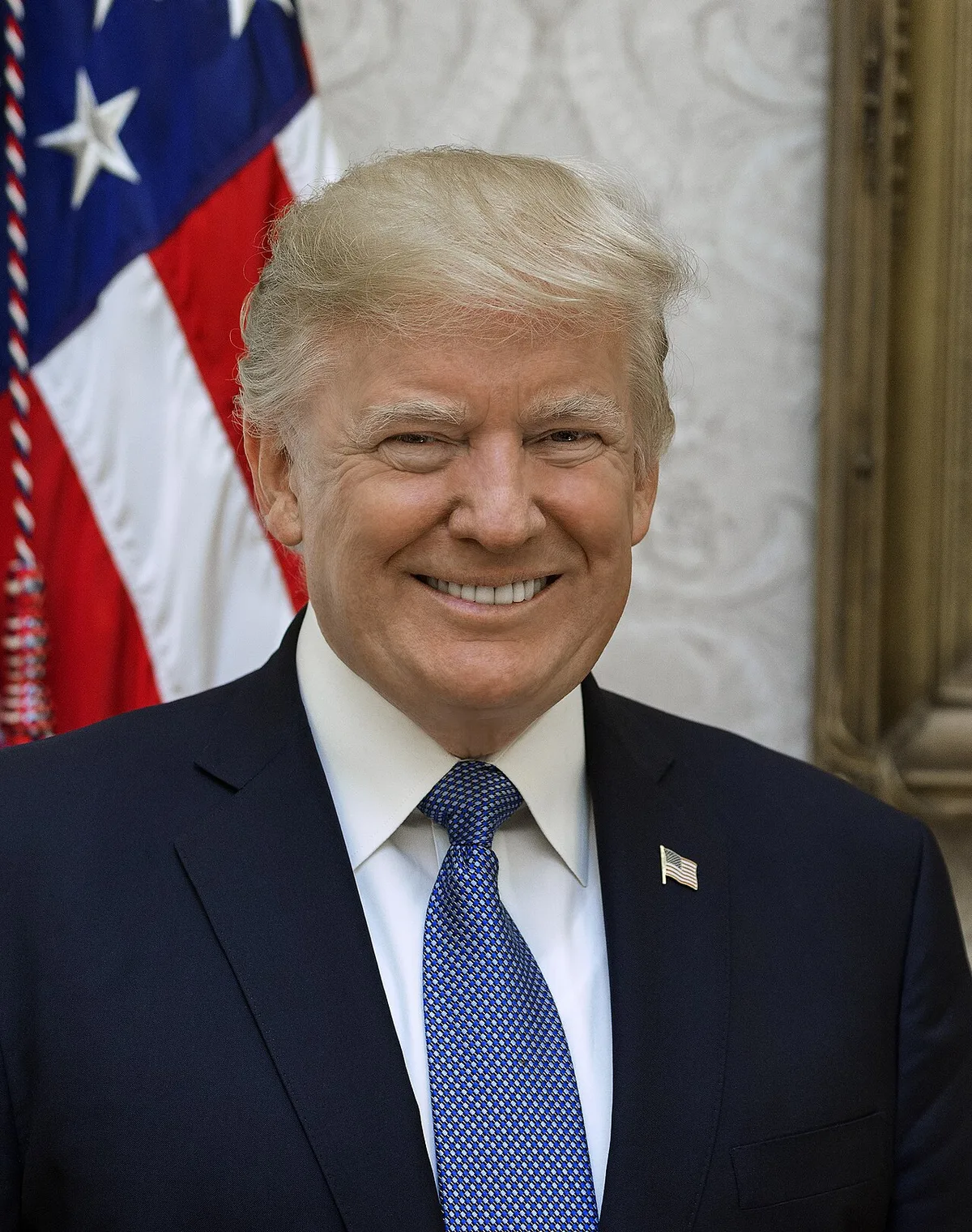 Studio portrait of Donald Trump in a dark suit with a red tie against a blurred background.