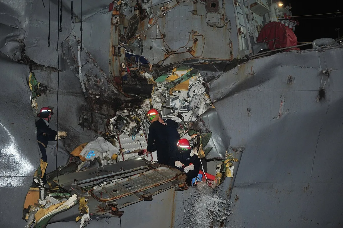 A damaged grey warship next to a large white oil tanker in the ocean.