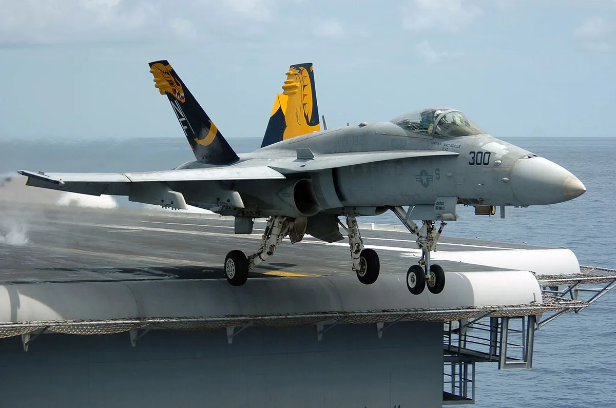A fighter jet taking off from the deck of a large aircraft carrier at sea.