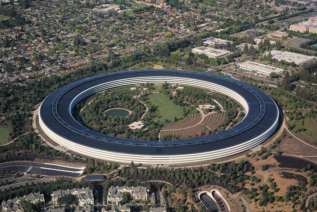 Aerial photograph of the circular Apple Park building surrounded by trees, with a solar-panel roof.
