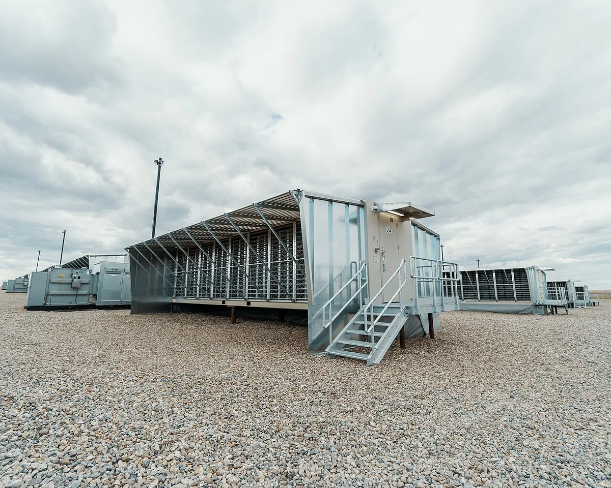 A white shipping-container-style modular Bitcoin mining data center unit at an outdoor facility.