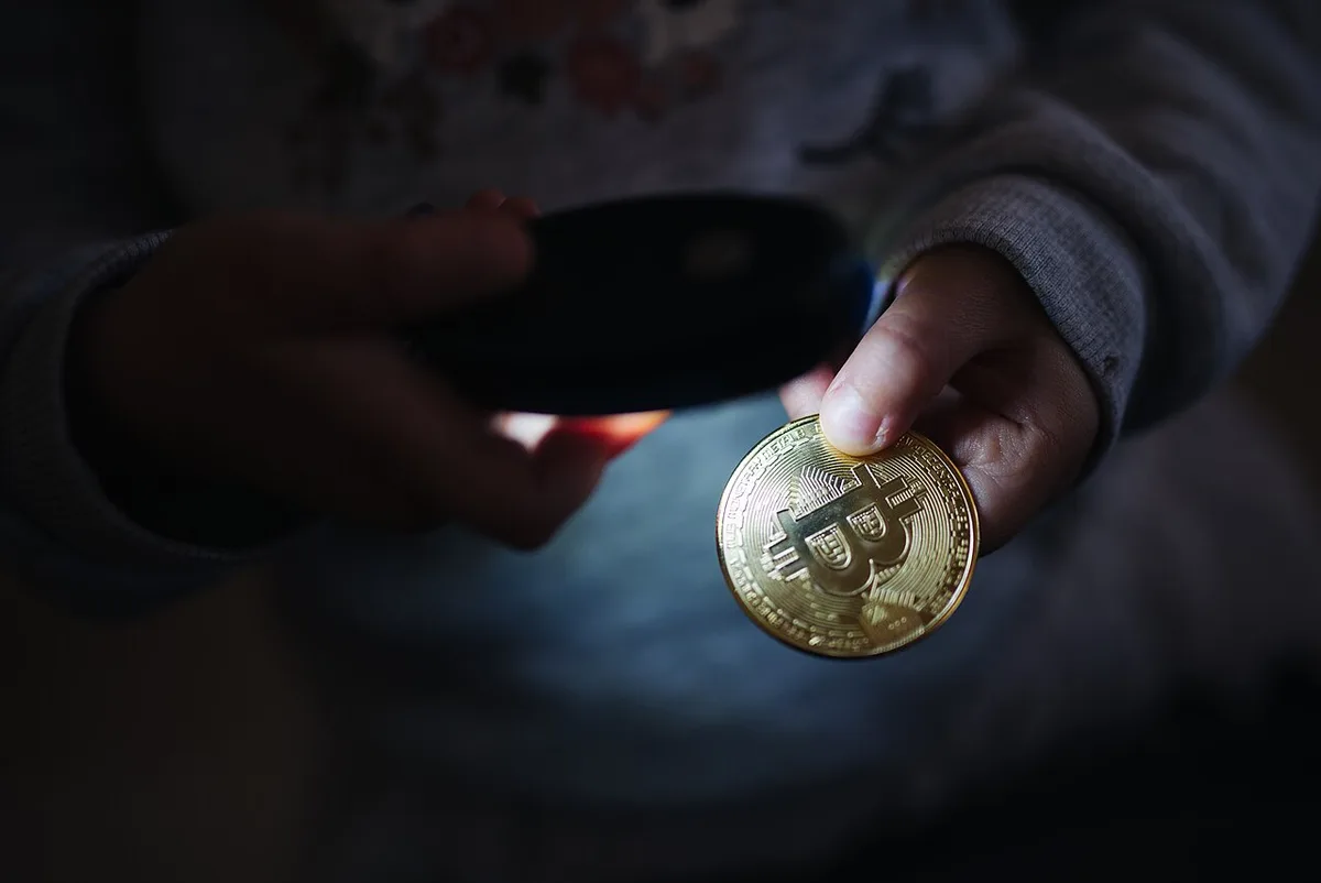 A child pointing a light at a physical Bitcoin coin.