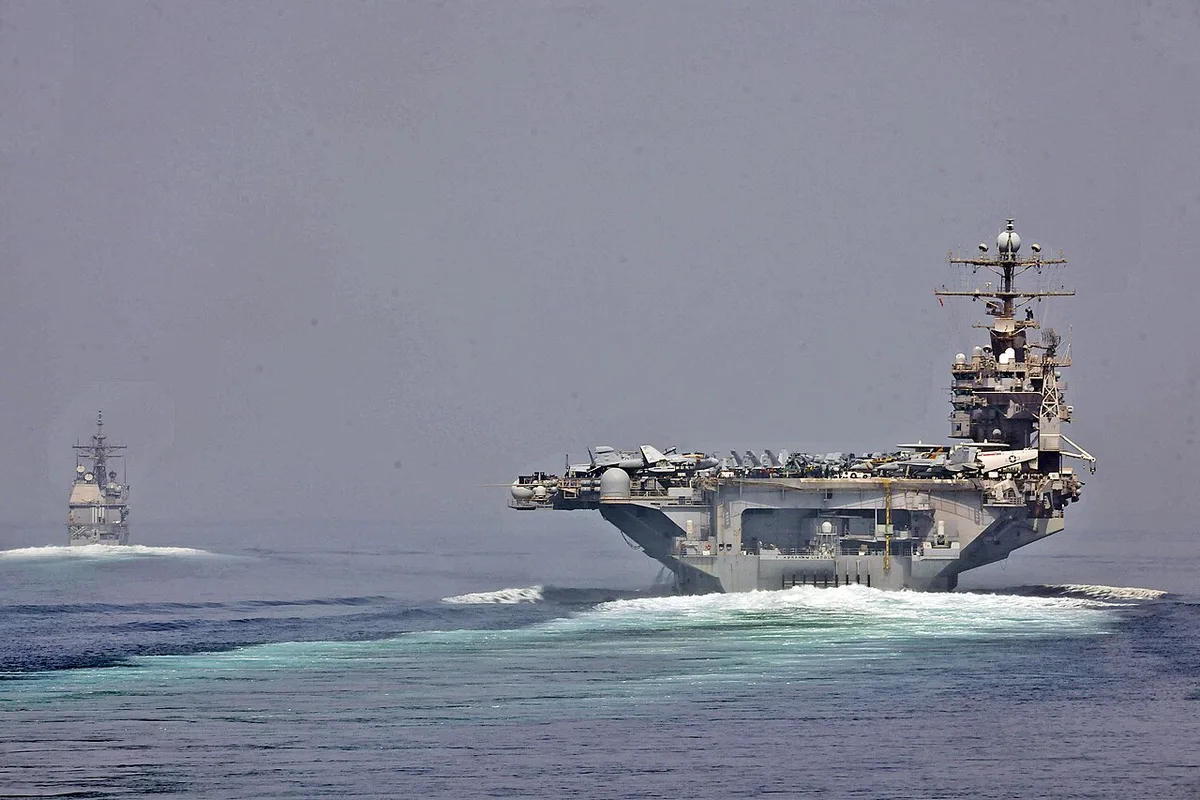 Two U.S. Navy ships, an aircraft carrier and a cruiser, sailing in formation on the ocean.